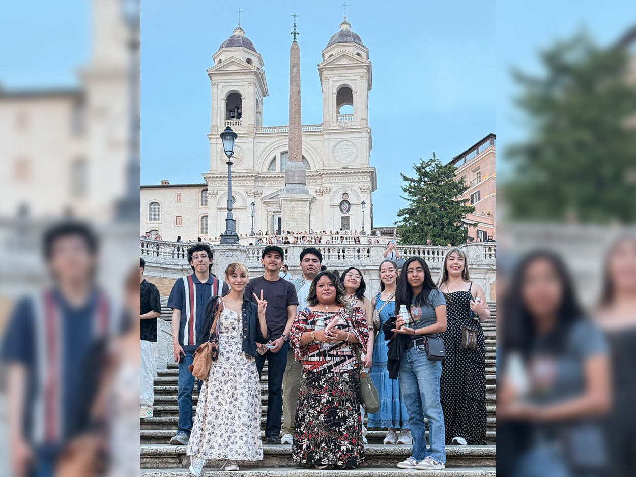 Group of students and travelers pose on the Spanish Steps in Rome, with the Trinità dei Monti church and its twin bell towers behind them.