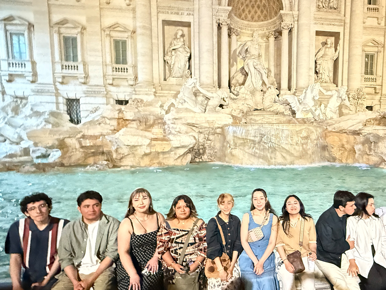 Group of students and travelers pose in front of the illuminated Trevi Fountain in Rome at night.