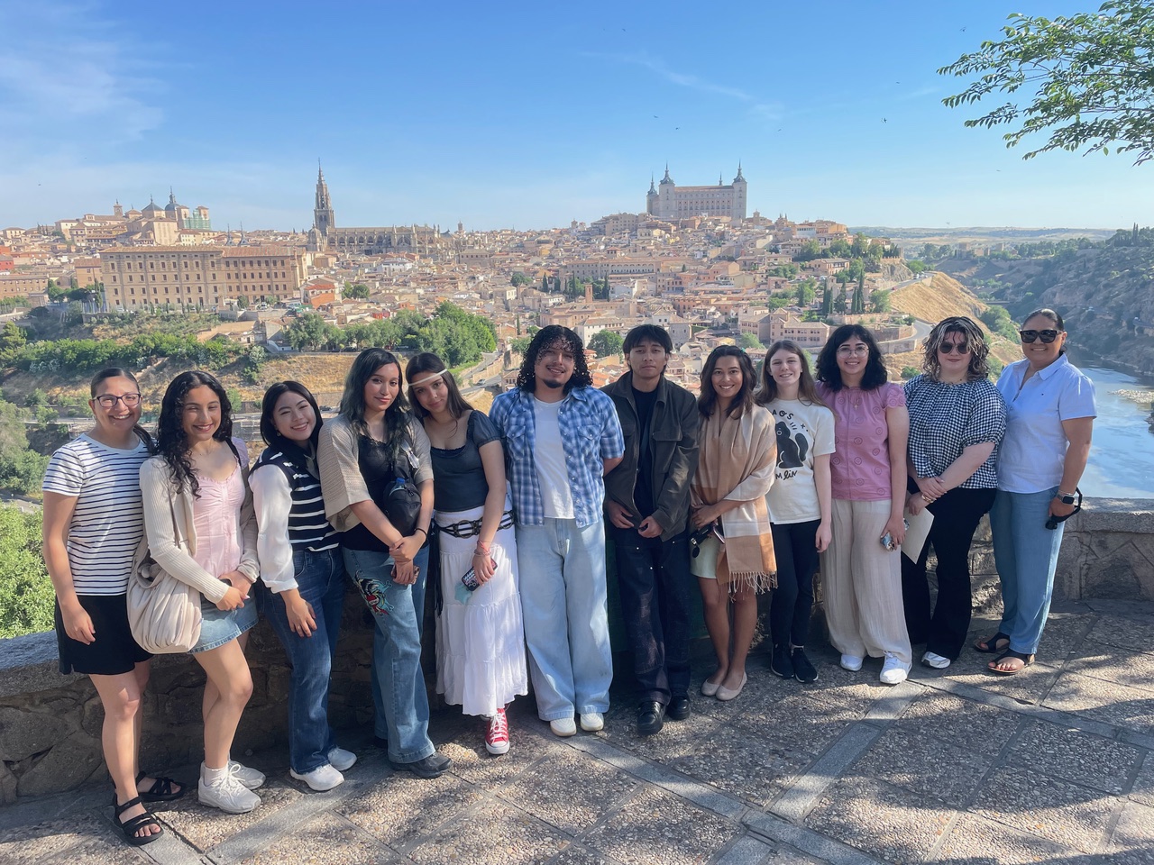 Group poses at a scenic overlook with the historic city of Toledo, Spain, spread across the hillside behind them.